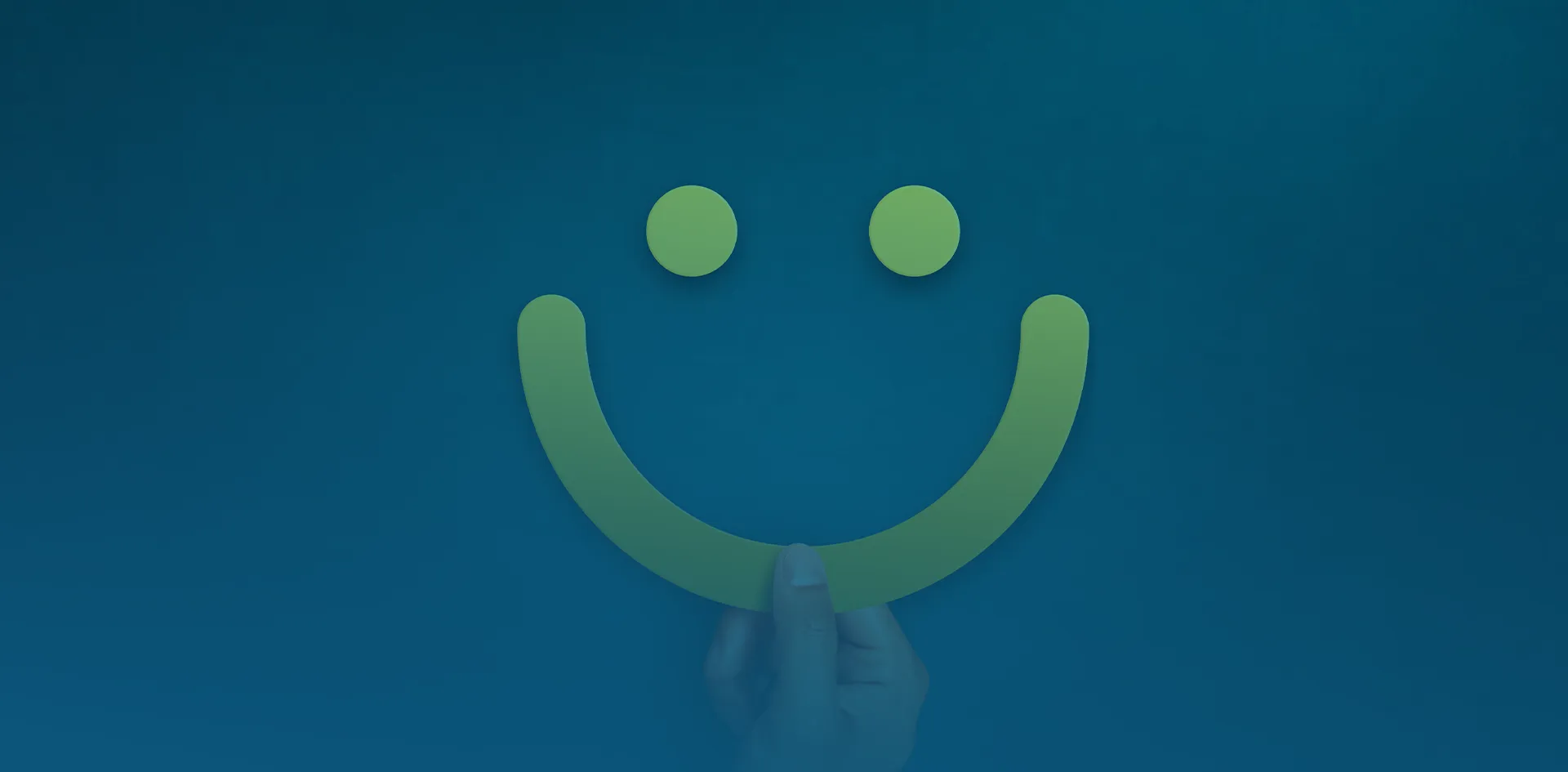 Eine Hand hält vor blauem Hintergrund einen grünen, lächelnden Mund aus Papier, der zusammen mit zwei Punkten ein Smiley-Gesicht bildet.